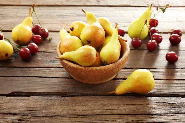 Las peras maduras y las cerezas en la mesa de madera de cerca