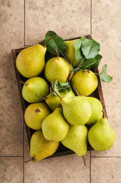 Peras Peras orgânicas frescas e doces com folhas em caixa de madeira ou cesta em fundo de ladrilho de pedra antiga Colheita de frutas no outono Vista superior Fundo de alimentos