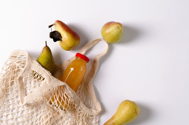 Peras de la variedad Trucha y conferencia con eco-sumka, una pequeña sobre fondo blanco. Hay una botella de vidrio con jugo de frutas en el eco-sup. copiando espacio, diseño plano