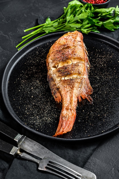 Perca de mar al horno servida en un plato redondo con perejil Superficie negra