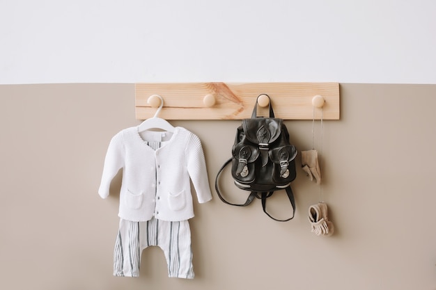 Percha de madera decorativa con bolso y traje de punto para niños en pared blanca y marrón