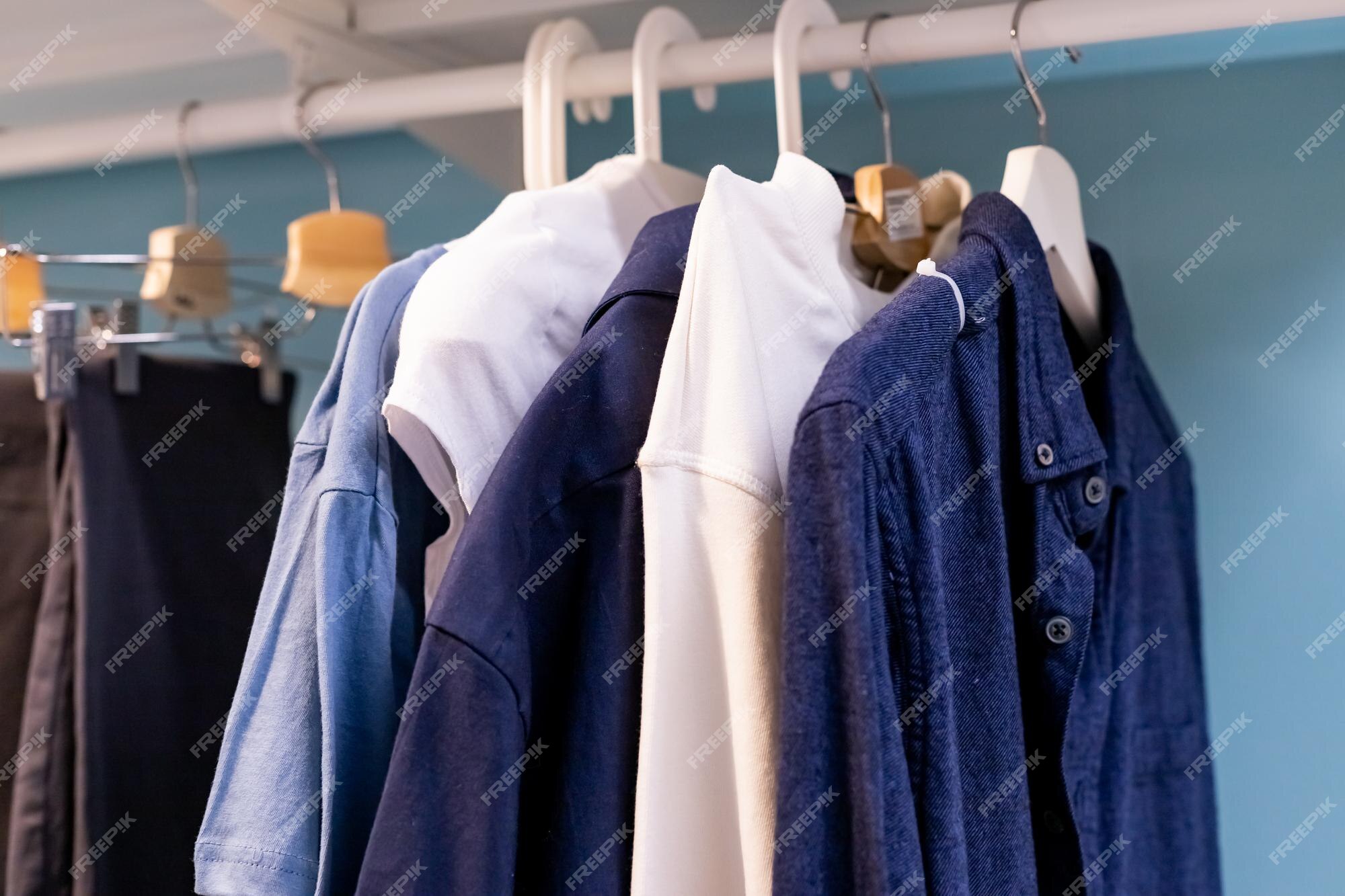 ropa diferente en el armario. camisas blancas y azules están colgadas en el riel en un armario madera casa. boutique de ropa | Foto Premium