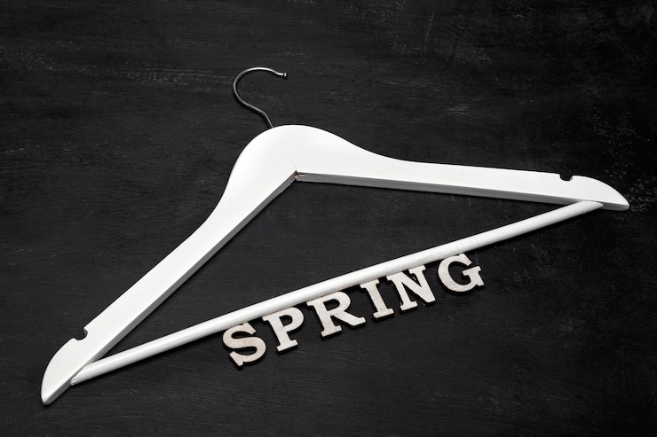 Foto perchero de madera blanca e inscripción primavera sobre fondo negro. colección de ropa de primavera.