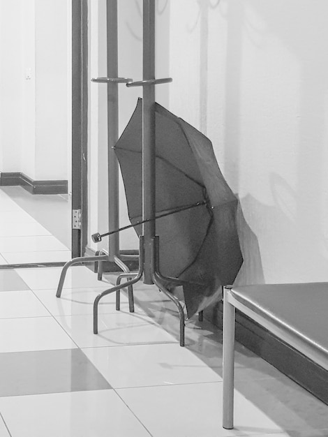 Perchero de madera con un paraguas abierto en una habitación vacía del pasillo de una clínica médica, vertical, blanco y negro