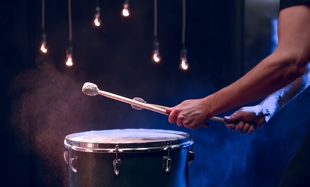 El percusionista toca con palos en el suelo tom bajo iluminación de estudio .. Concierto y concepto de interpretación.