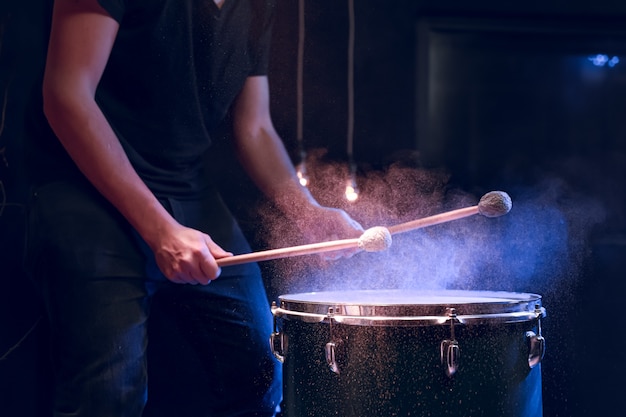 El percusionista toca con palos en el suelo tom bajo iluminación de estudio .. Concierto y concepto de interpretación.