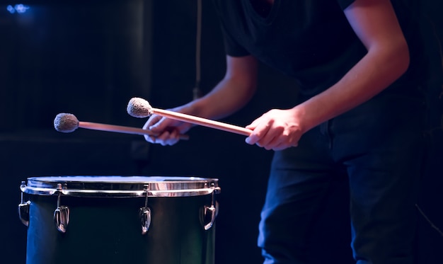 El percusionista toca con palos en el tom de suelo en una habitación oscura con una hermosa iluminación. Concepto de concierto y actuación.