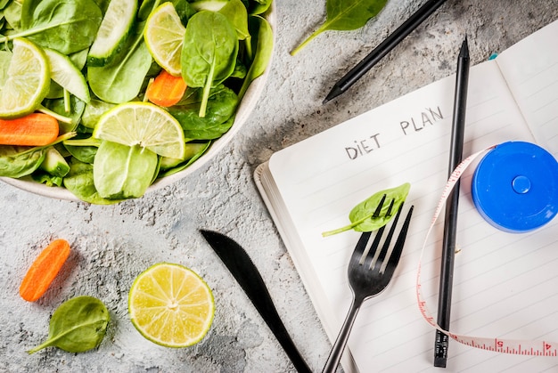 Perda de peso de plano de dieta perder conceito, salada de legumes frescos com garfo, faca, bloco de notas, vista superior de espaço de cópia de tabela de pedra cinza