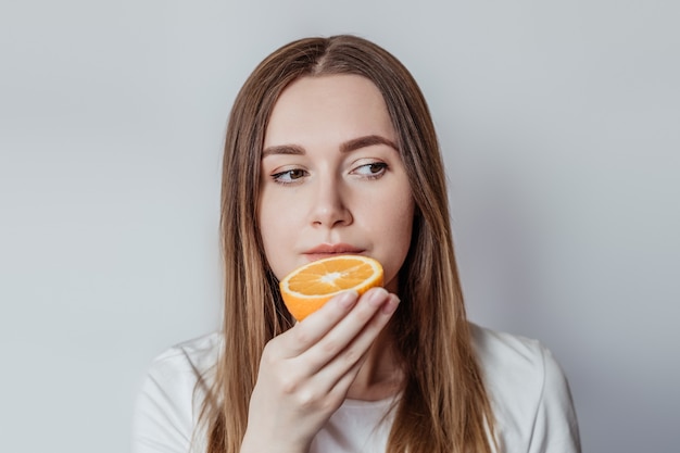 Perda do conceito de cheiro. Jovem caucasiana segurando uma laranja perto do nariz isolada