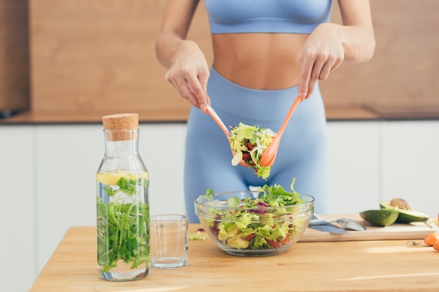 perder a foto de uma garota bonita preparando salada de vegetais e abacate na cozinha