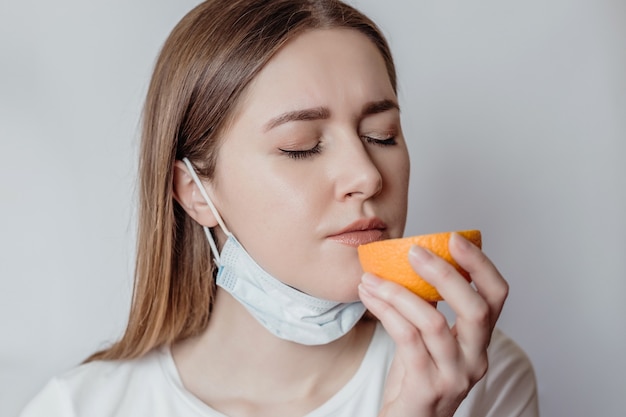 Pérdida del concepto de olfato. Mujer joven caucásica en una máscara médica oliendo una naranja