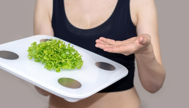 pérdida de peso concepto de bienestar y nutrición mujer joven sosteniendo hojas de ensalada en báscula corporal