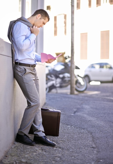 Foto pérdida de trabajo y hombre en la calle despedido y leyendo carta de desempleo en la acera de la ciudad ansiedad salud mental y triste hombre de negocios en la carretera con aviso de terminación maletín y bolso rosa