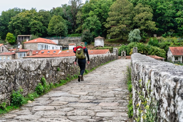 Peregrino camino de Santiago pasando un puente medieval en Galicia