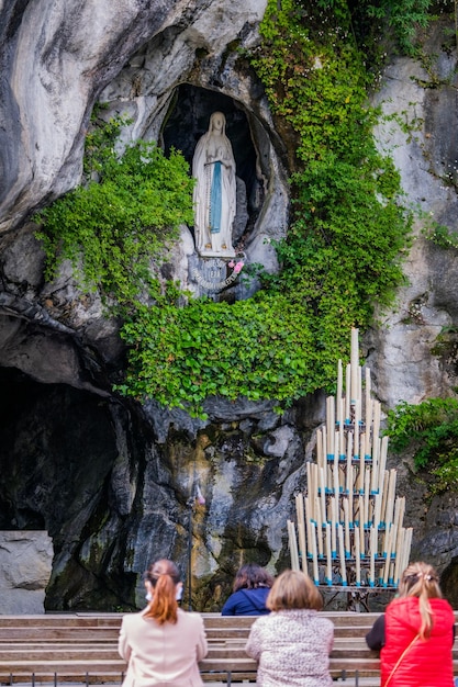 Peregrinos rezando frente a la Gruta de Lourdes con la estatua de Bernadette Soubirous en Francia