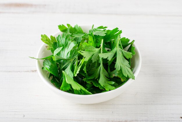 Perejil fresco en un plato sobre un fondo blanco de madera Ingrediente de cocina