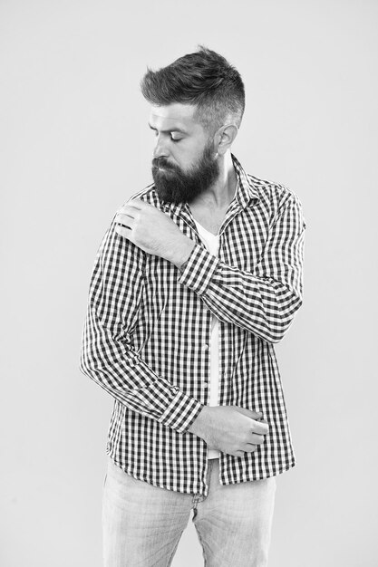 Perfectamente imperfecto Hombre de moda desempolvando motas de su manga sobre fondo amarillo Hombre barbudo en estilo de moda hipster Hipster de moda con barba larga con ropa de moda casual Tendencia de moda