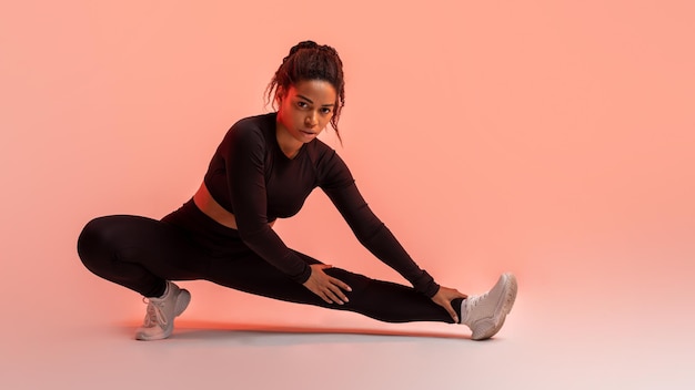 Perfeição de estúdio em forma de senhora negra dominando sua rotina de exercícios esticando pernas pêssego neon