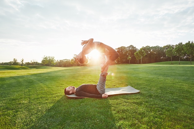 Perfekte Flexibilität, schönes Paar, das zusammen im Freien an einem sonnigen Morgenmann Acro-Yoga praktiziert