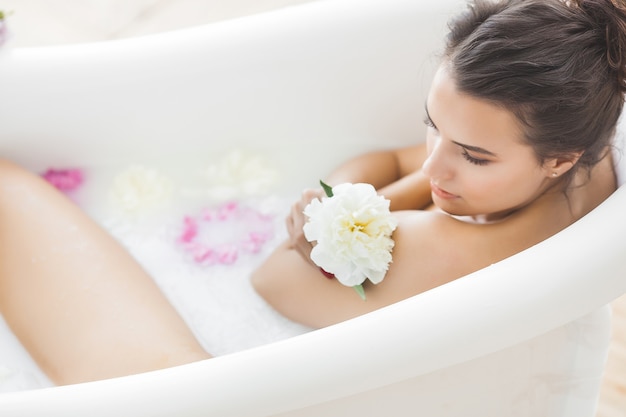 Perfekte Frau, die mit Blumen und Milch badet