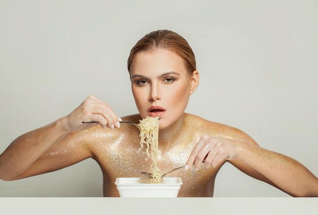 Perfekte Frau in goldenem Glanz, die Instant-Nudeln auf weißem Hintergrund isst.