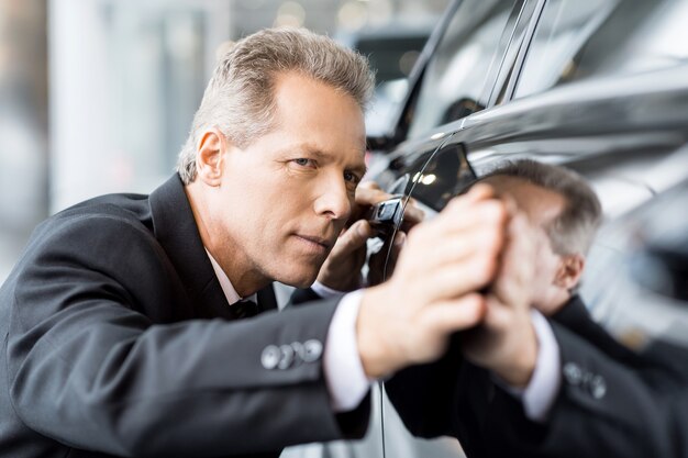 Perfekte Linien. Reifer Geschäftsmann mit grauen Haaren, der Auto im Autohaus untersucht