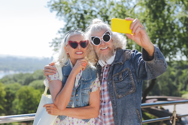 Perfekter Stil. Erfreute alte Menschen, die eine Sonnenbrille tragen, während sie zusammen für das Foto posieren