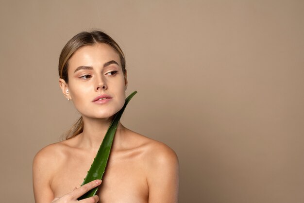 Perfektes Gesicht eines brünetten Mädchens und grüner Aloe auf beigefarbenem Hintergrund. Hautpflege, feuchtigkeitsspendend.