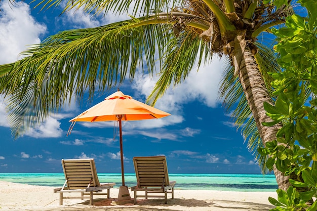 Perfektes Paar Reiseziel landschaftlich, Stühle Sonnenschirm und Palmblätter. Sommerreise Flitterwochen Strand