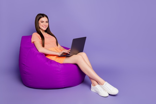 Perfil alegre senhora sentada confortável beanbag navegando no caderno