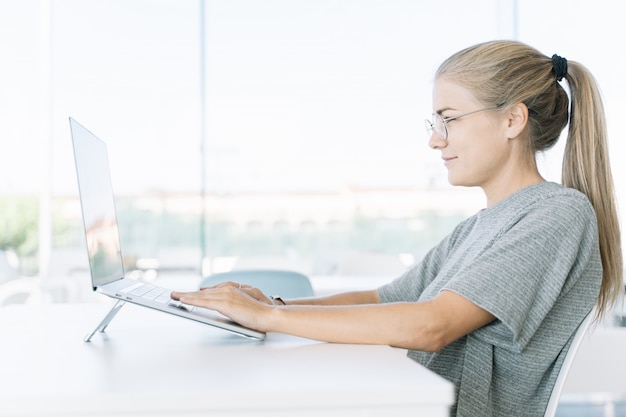 Perfil de una chica rubia con gafas trabajando con un portátil