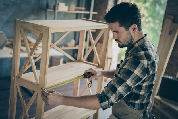 Perfil chico guapo edificio estantería de libros de diseño moderno industria de madera artesanal midiendo la longitud de la distancia entre los departamentos del taller en el interior