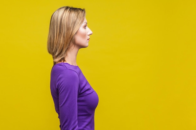 Perfil de jovem empresária confiante em elegante vestido roxo, olhando bem com expressão inteligente séria, espaço de cópia vazio para propaganda. tiro de estúdio interno isolado em fundo amarelo