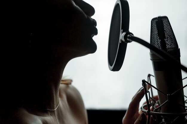 Foto perfil de silhueta escura de uma jovem mulher com ombros nus, cantando no microfone