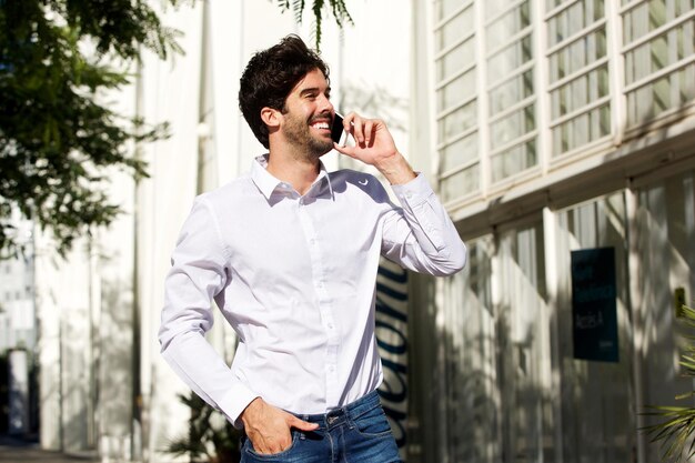 Perfil de um homem sorridente de pé e falando ao telefone na cidade