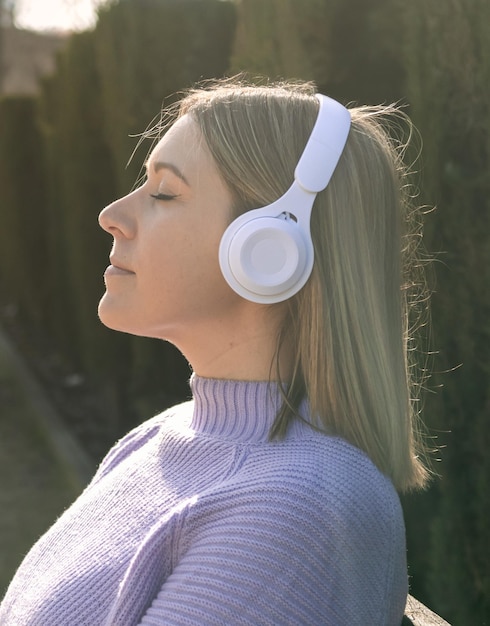 Perfil de uma mulher com fones de ouvido brancos ouvindo música no parque