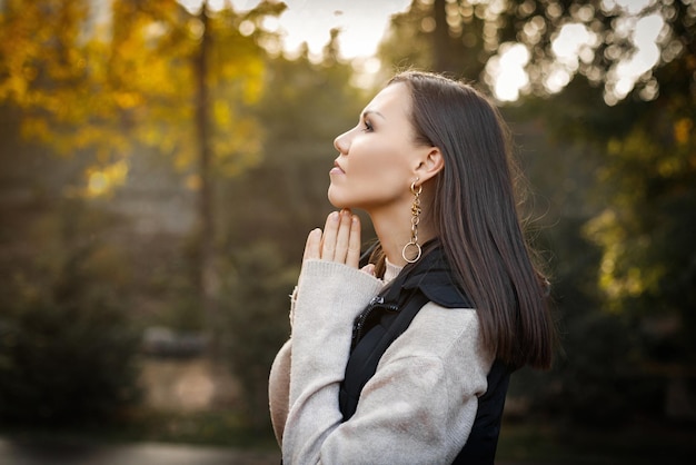 Perfil de uma mulher séria e pensativa com as mãos perto do rosto no outono ao ar livre em jaqueta bege e jaqueta sem mangas