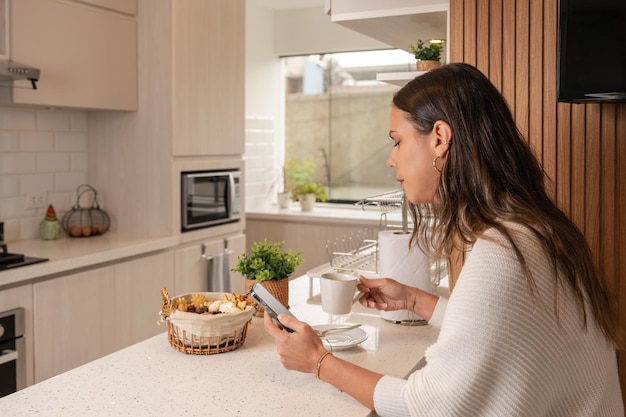 Perfil de uma mulher tomando café da manhã e usando o celular em uma nova cozinha