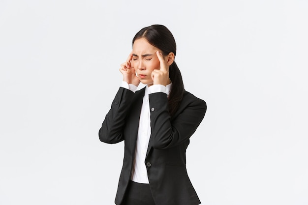 Perfil de empresaria asiática en traje negro que tiene migraña, toca las sienes y hace muecas de doloroso sentimiento en la cabeza. Gerente de oficina femenina que tiene dolor de cabeza, necesita analgésicos, fondo blanco.
