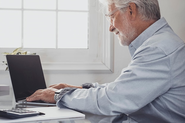 Perfil de feliz viejo hombre de negocios caucásico o contador escribiendo en el teclado de la computadora portátil y haciendo trabajo en línea Confiado hombre senior sonriente escribiendo en el teclado trabajando en la oficina en casa