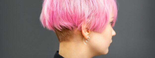 Perfil de una hermosa joven caucásica con un peinado corto de bob rosa sobre fondo gris oscuro