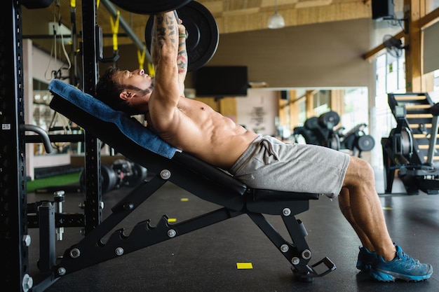 Perfil de un hombre haciendo ejercicios de press de banca en un gimnasio.