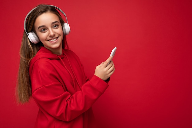 Perfil lateral de una chica morena bonita sonriente positiva con sudadera con capucha roja aislada en rojo