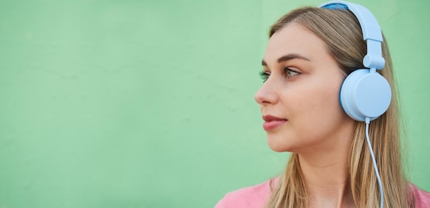 Perfil de una mujer joven con auriculares azules escuchando música en un fondo de pared verde