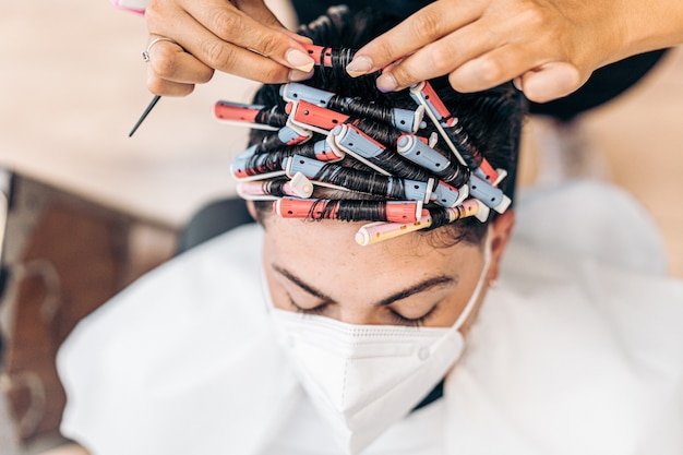 Perfil de una peluquera rubia arreglando los rizos del cabello de un hombre con máscara con un peine