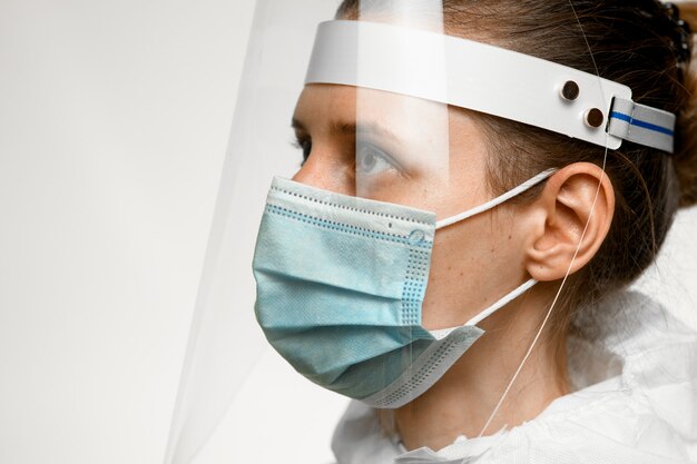 Perfil de primer plano de mujer joven en máscara médica y pantalla protectora en la cabeza