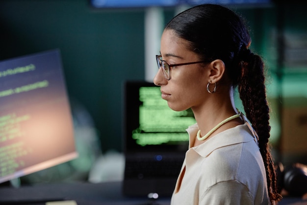 Perfil de programadora de Oriente Medio con gafas usando computadora en el lugar de trabajo