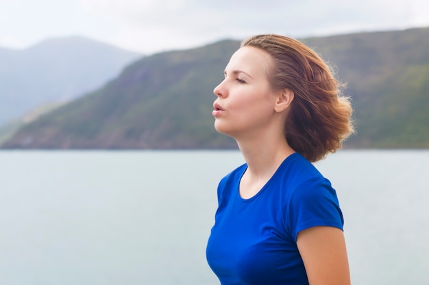 Perfil, vista lateral retrato de mujer relajada respirando profundamente aire fresco en el mar, el océano en las montañas. Calma joven pelirrojo jengibre chica relajante, meditando al aire libre haciendo ejercicios de respiración. Copia espacio