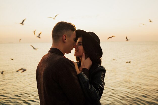 Perfiles de pareja romántica con estilo mirando el uno al otro en el fondo de la puesta de sol y gaviotas volando.