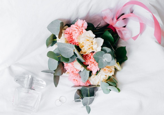 Perfume, anillos y un hermoso ramo de novia en la cama.